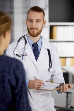 Dost canlısı kızıl sakallı doktor ve hasta kadın güneşli klinikte otururken sağlık muayenesini tartışıyorlar. Tıp konsepti