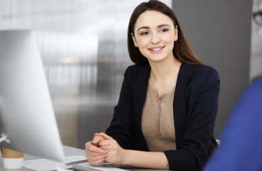 Genç ve güzel bir iş kadını, modern bir ofiste masada otururken iş arkadaşıyla konuşuyor. İş başarısı kavramı