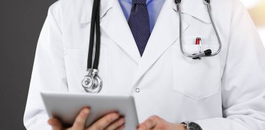Bilinmeyen erkek doktor, güneşli klinikte dururken elinde tablet bilgisayar kullanıyordu. Coronavirus salgını sırasında ilaç konsepti. Covid 2019