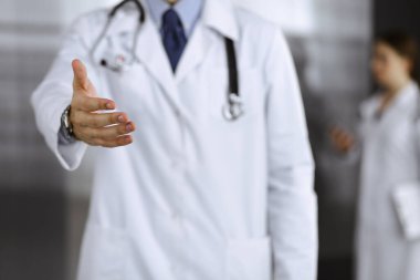 Bilinmeyen bir adam-doktor ayakta duruyor ve modern klinikte yardım eli uzatıyor. Kadın meslektaşının doktor geçmişinde acelesi var. Tıp konsepti