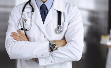 Koruyucu maskeli kimliği belirsiz erkek doktor klinikte kollarını kavuşturmuş duruyor. Coronavirus salgını sırasında ilaç konsepti. Covid 2019