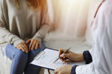 Kadın-doktor ve hasta yakın plan çekimleri. İçeride otururken sağlık muayenesini tartışıyorlar. Coronavirus salgını ve kendini izolasyon karantinası sırasında evde kal. Covid 2019