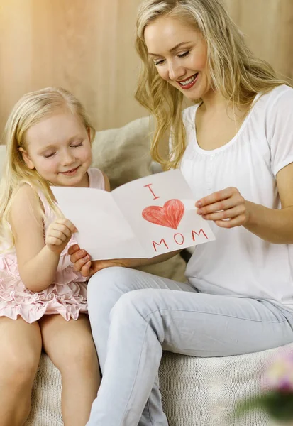 Bonne fête des mères dans un appartement ensoleillé. Enfant fille félicite maman et donne sa carte postale avec le dessin du cœur. Concept de famille — Photo