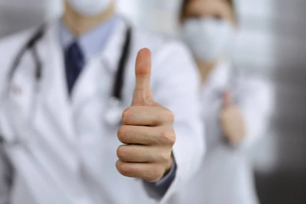 Unknown man-doctor and woman standing straight as a team and showing Ok sign with thumbs up in modern clinic. Medicine concept during Coronavirus pandemic. Covid 2019 — Stock Photo, Image