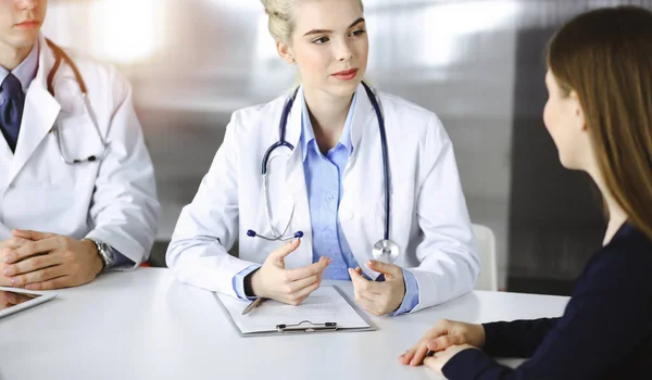 Mulher-médico com colega do sexo masculino estão consultando mulher paciente enquanto sentado na mesa na clínica moderna. Serviço médico perfeito, conceito de medicina — Fotografia de Stock