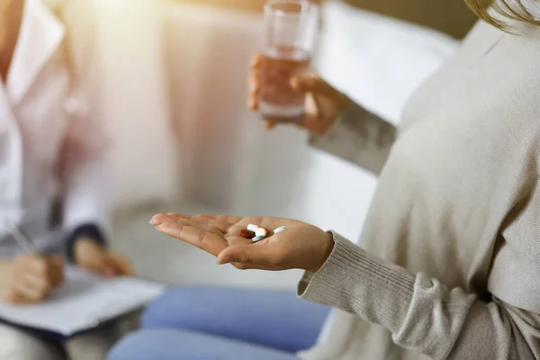 Close-up woman-patient holding pills near her doctor, time to take medications for headache. Stay at home concept during Coronavirus pandemic and self isolation quarantine. Covid 2019