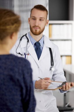 Dost canlısı kızıl sakallı doktor ve hasta kadın güneşli klinikte otururken sağlık muayenesini tartışıyorlar. Tıp konsepti