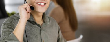 Kulaklıklı genç adam modern güneşli bir ofiste otururken bir müşteriyle konuşuyor. İş yerindeki çağrı merkezi operatörleri