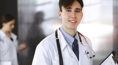 Modern klinikte dostane genç bir erkek doktor elinde bir panoyla dikiliyor. Bayan meslektaşım, doktorların arka planında ilaç kayıtları doldurmakla meşgul. Tıp konsepti