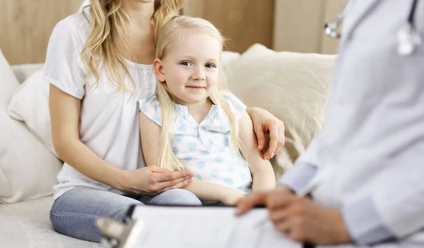 Doctor y paciente. Pediatra usando portapapeles mientras examina a la niña con su madre en casa. Feliz lindo niño caucásico en el examen médico. Concepto de medicina — Foto de Stock