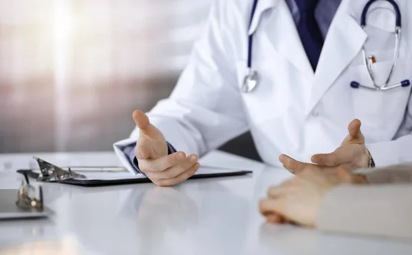 Médico masculino desconocido y mujer paciente discutiendo algo mientras está sentado en una clínica oscura, resplandor de luz en el fondo. Primer plano de las manos — Foto de Stock