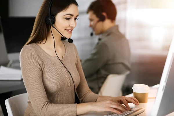 Operadores de centro de llamadas en el trabajo. Dos jóvenes con auriculares están hablando con los clientes, mientras están sentados en una oficina soleada — Foto de Stock