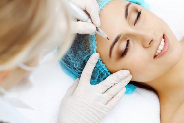 Kadın yüzüne kaş dövmesi yapan profesyonel bir güzellik uzmanı. Güzellik salonunda kalıcı kaş makyajı, yakın çekim. Kozmetoloji tedavisi