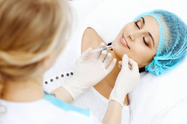 Profesyonel kozmetik uzmanı yüzüne ve dudaklarına iğne yapıyor. Genç bir kadın, yüz hatları ya da büyütme için doldurucu iğneyle doldurulur. Yaşlanma, gençleşme ve hidrasyon prosedürleriyle yüzleş