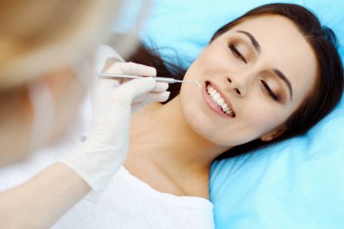 Genç bayan hasta dişçi muayenehanesini ziyaret ediyor. Sağlıklı, beyaz dişleri olan güzel bir kadın diş hekimliğinde çalışırken ağız muayenesi sırasında diş sandalyesinde oturuyor.