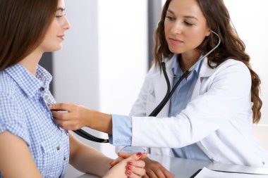 Elinde steteskop olan bir doktor kadın hastasını muayene ediyor. Sağlık, kardiyoloji ve tıp kavramları