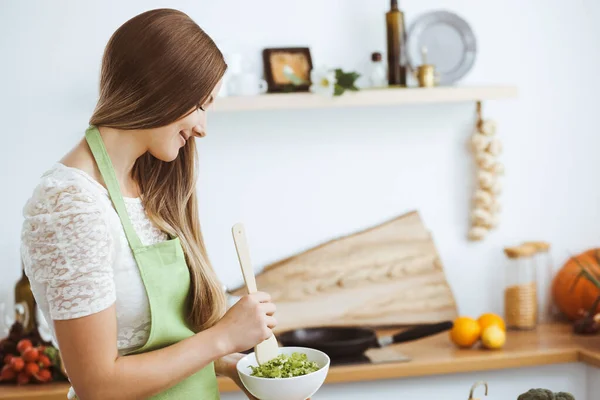 앞치마를 입은 아름다운 여인이 부엌에서 요리를 하고 있다. 신선 한 야채 샐러드를 썰고 있는 주부 — 스톡 사진