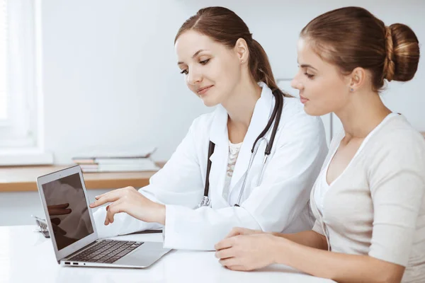 Médico e paciente estão sentados e discutindo os resultados do exame de saúde ao usar o computador portátil. Saúde, medicina e boas notícias conceitos — Fotografia de Stock