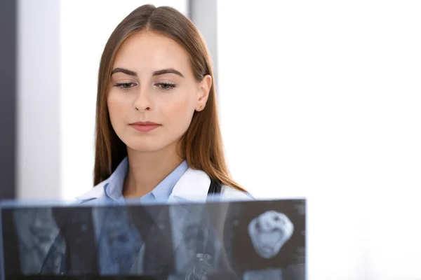 Doctor woman examining x-ray picture while standing near window in hospital. Surgeon or orthopedist at work. Medicine and healthcare concept