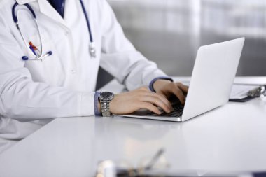 Bilinmeyen bir erkek doktor klinikte dizüstü bilgisayarla yakın planda çalışıyor. İşteki genç doktor. Mükemmel sağlık hizmeti, tıp konsepti