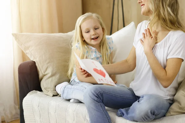 Glücklicher Muttertag in sonniger Wohnung. Die Tochter gratuliert der Mutter und überreicht ihr eine Postkarte mit Herzzeichnung. Familienkonzept — Stockfoto
