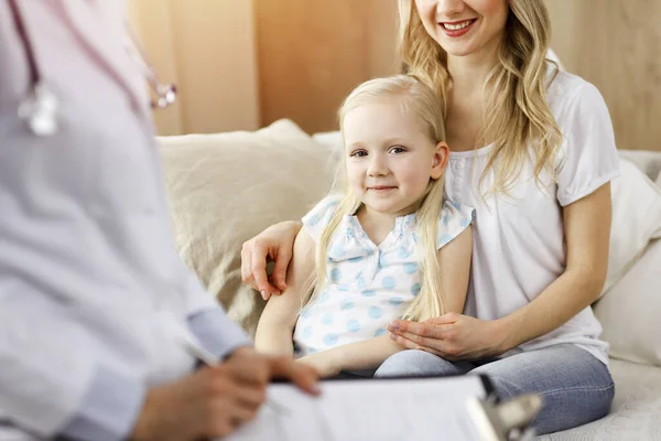 Doctor and patient in sunny room. Pediatrician using clipboard while examining little girl with her mother at home. Medicine concept — Stock Photo, Image