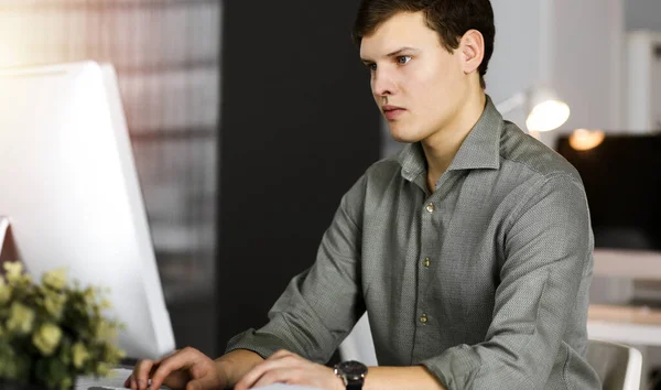 Молодой бизнесмен, работающий за компьютером, сидит за столом в офисе. Хедшот портрет человека — стоковое фото