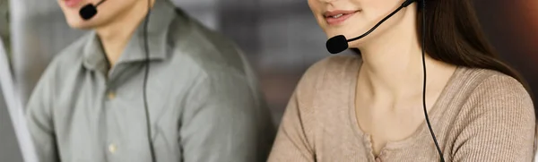 Dos personas sonrientes con auriculares están hablando con los clientes, mientras están sentados en el escritorio en la soleada oficina moderna —  Fotos de Stock