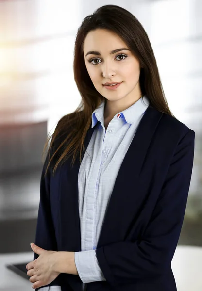 Intelligent young business woman in a blue jacket is standing at her workplace. Portrait of a specialist in sunny office