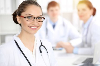 Mutlu gülümseyen kadın doktor tıbbi personelle toplantıda oturup kameraya bakıyor. Tıp konsepti