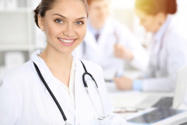 Mutlu gülümseyen kadın doktor tıbbi personelle toplantıda oturup kameraya bakıyor. Tıp konsepti