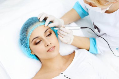 Kadın yüzüne kaş dövmesi yapan profesyonel bir güzellik uzmanı. Güzellik salonunda kalıcı kaş makyajı, yakın çekim. Kozmetoloji tedavisi