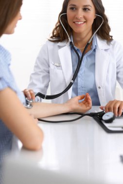 Doktor, hastane bürosundaki masada otururken kan basıncını ölçüyor. Tıp ve sağlık konularında kardiyoloji