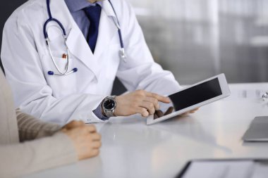 Bilinmeyen erkek doktor ve hasta kadın klinikte oturup tablet bilgisayar kullanırken bir şeyler tartışıyorlar. Hastanedeki en iyi sağlık hizmeti, ilaç, salgın durdurma.