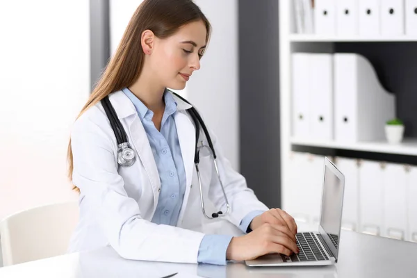 Médico mujer escribiendo en el ordenador portátil mientras está sentado en el escritorio en la oficina del hospital. Médico trabajando. Concepto de medicina y salud — Foto de Stock