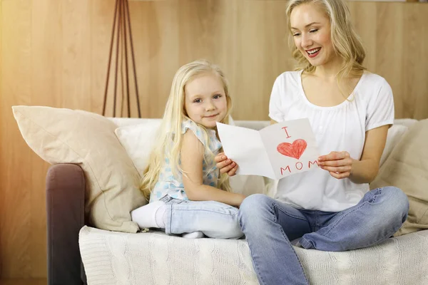 Bonne fête des mères dans un appartement ensoleillé. Enfant fille félicite maman et donne sa carte postale avec le dessin du cœur. Concept de famille — Photo