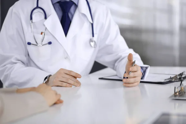 Unknown male doctor and patient woman discussing something while sitting in clinic and using clipboard. Best medical service in hospital, medicine, pandemic stop — Stock Photo, Image