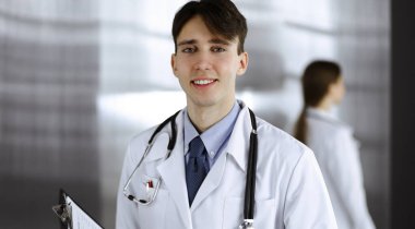 Modern klinikte dostane genç bir erkek doktor elinde bir panoyla dikiliyor. Bayan meslektaşım, doktorların arka planında ilaç kayıtları doldurmakla meşgul. Tıp konsepti