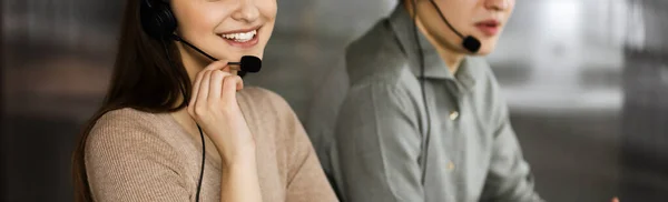 Twee jonge mensen in headsets praten met de klanten, terwijl ze aan het bureau zitten in een kantoor. Focus op de vrouw. Exploitanten van callcenters aan het werk — Stockfoto