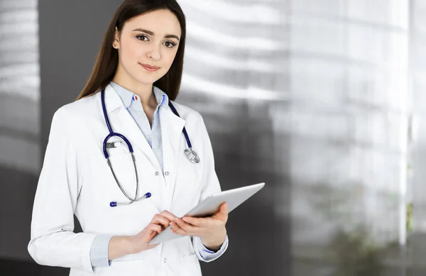 쾌활하게 똑똑 한 여성 - 의사는 그녀가 병원에 서 있는 동안그녀의 손에 태블릿 컴퓨터를 쥐고 있습니다. 친절 한 의사 가 직장에 있는 모습. 병원에서의 완벽 한 의료 서비스 — 스톡 사진