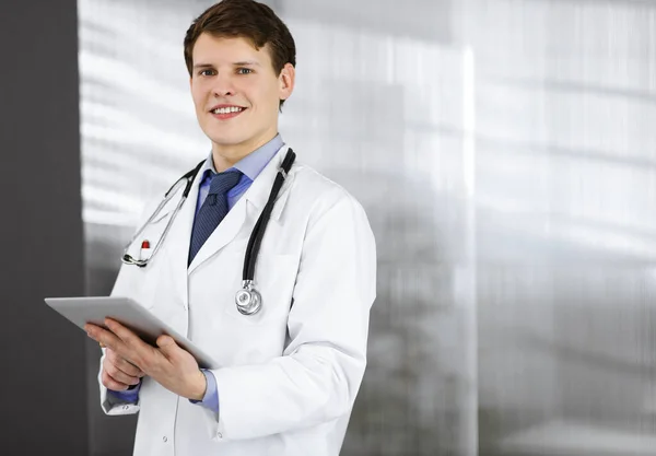친절 한 젊은 의사가 컴퓨터 태블릿에 있는 정보를 확인하고 있습니다. 전문 의사 가 병원에서 일하는 모습. 의학적 개념 — 스톡 사진