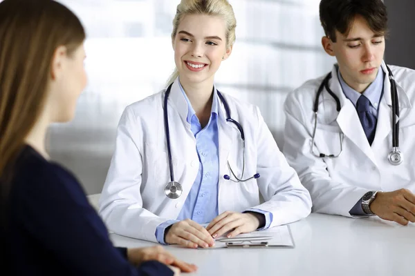 Γυναίκα-γιατρός με αρσενικό συνάδελφο συμβουλεύονται ασθενή γυναίκα, ενώ κάθεται στο γραφείο στη σύγχρονη κλινική. Τέλεια ιατρική υπηρεσία, ιατρική έννοια — Φωτογραφία Αρχείου