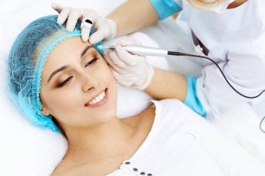 Kadın yüzüne kaş dövmesi yapan profesyonel bir güzellik uzmanı. Güzellik salonunda kalıcı kaş makyajı, yakın çekim. Kozmetoloji tedavisi