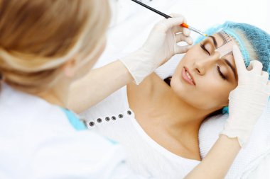 Profesyonel güzellik uzmanı kozmetik cetvel kullanarak kaş çizgisini düzeltecek. Güzellik salonunda kalıcı kaş makyajı, yakın çekim. Kozmetoloji tedavisi