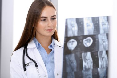 Doktor kadın hastanenin penceresinin yanında dikilirken röntgen filmini inceliyor. Cerrah ya da ortopedist. Tıp ve sağlık hizmetleri kavramı