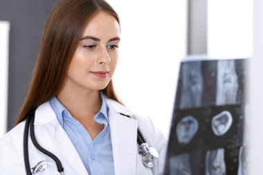 Doktor kadın hastanenin penceresinin yanında dikilirken röntgen filmini inceliyor. Cerrah ya da ortopedist. Tıp ve sağlık hizmetleri kavramı