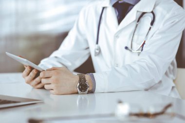 Bilinmeyen erkek doktor klinikteki tablet bilgisayarla yakın planda çalışıyor. İşteki genç doktor. Mükemmel sağlık hizmeti, tıp konsepti