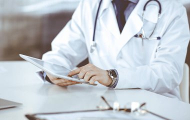 Bilinmeyen erkek doktor klinikteki tablet bilgisayarla yakın planda çalışıyor. İşteki genç doktor. Mükemmel sağlık hizmeti, tıp konsepti