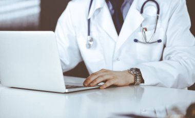 Bilinmeyen bir erkek doktor klinikte dizüstü bilgisayarla yakın planda çalışıyor. İşteki genç doktor. Mükemmel sağlık hizmeti, tıp konsepti