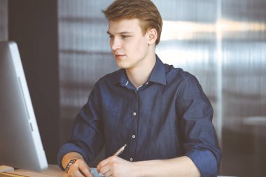 Genç sarışın işadamı iş yerinde bilgisayarla strateji düşünüyor. Girişim işi, başarı için çok çalışmak ve zamanın dışında çalışmak demektir.